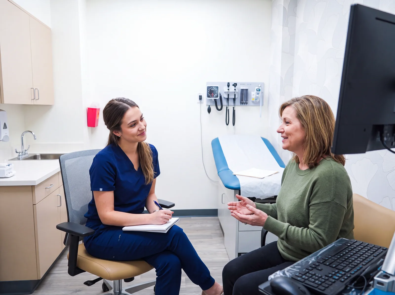 A clinician in scrubs talking with a woman during a private office conversation