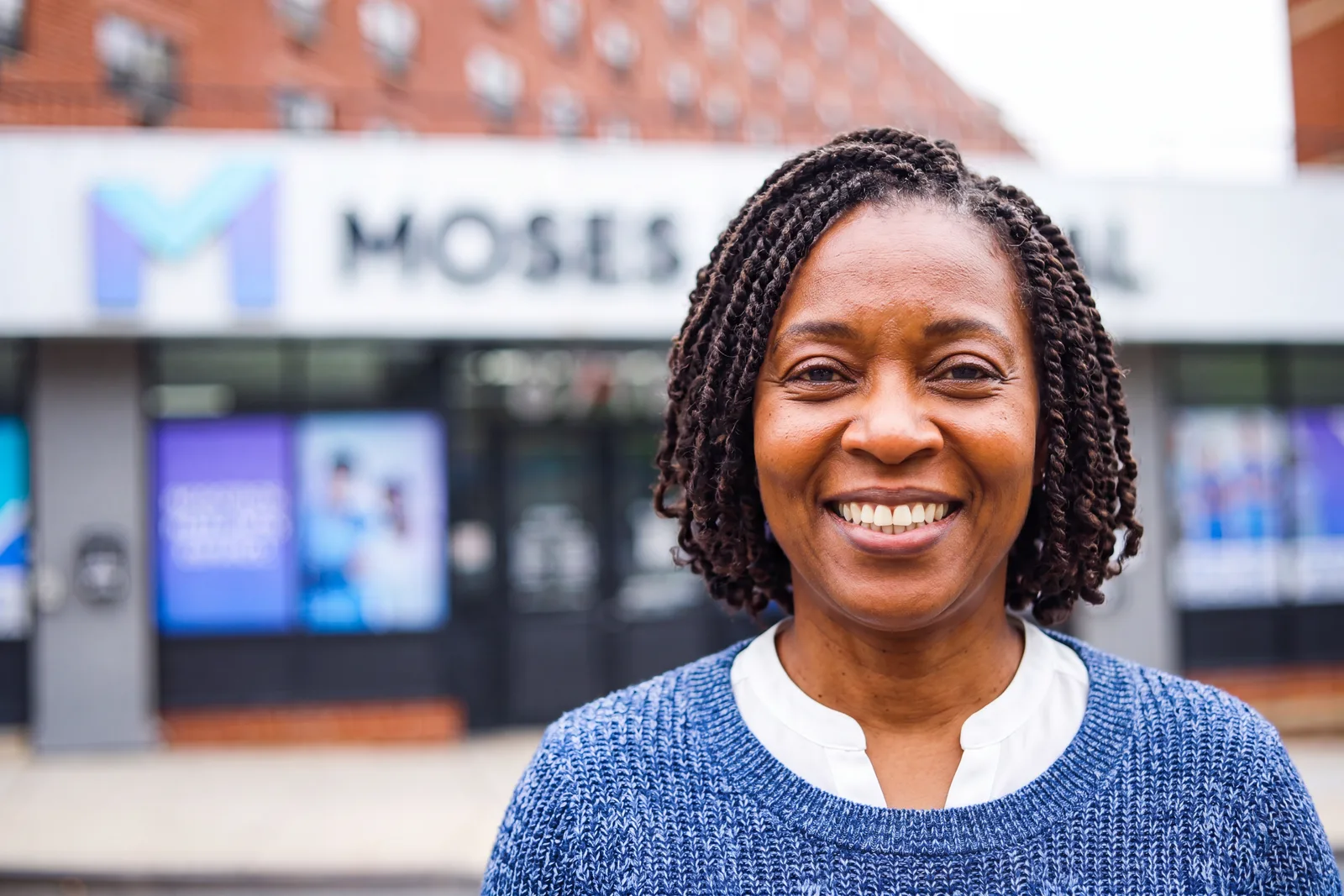 A smiling woman outside the Moses Medical storefront on Westchester Avenue